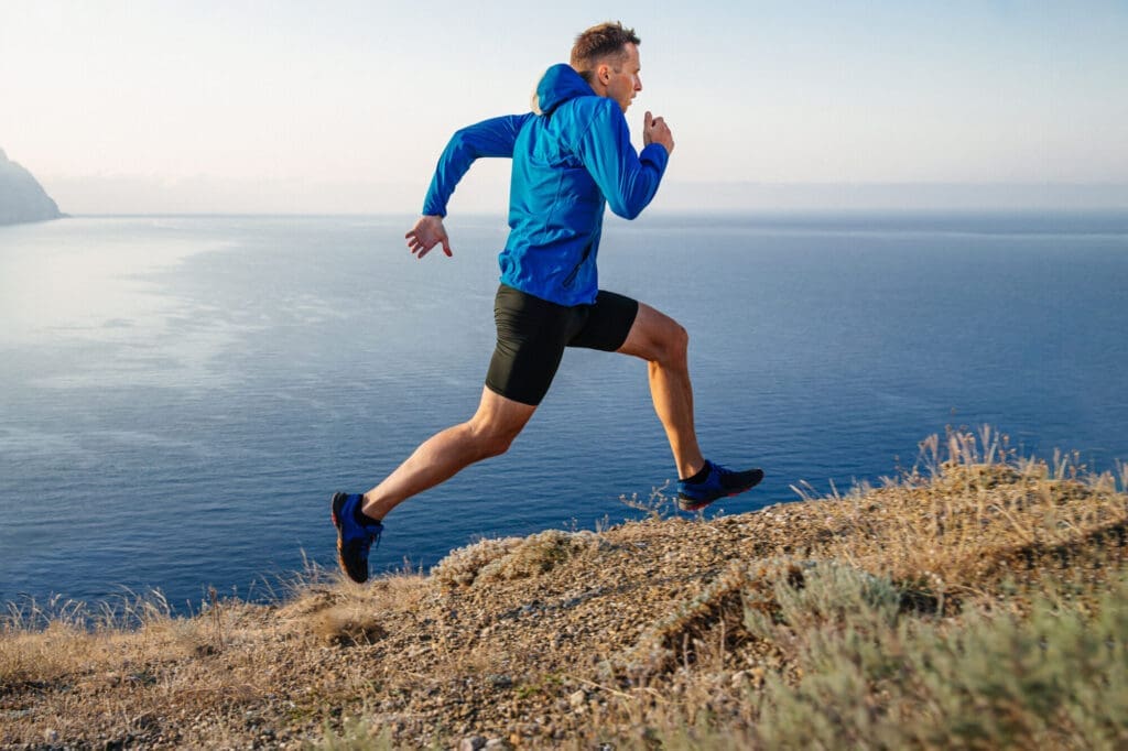 Male runner on an uphill clifftop trail in a blue jacket and… — Le Sentier des Pins in Ramatuelle
