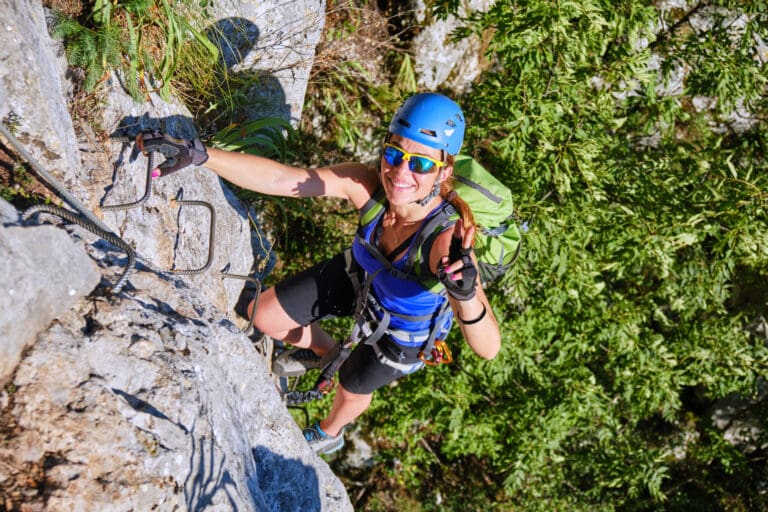 Smiling tourist giving a victory sign while climbing – Via ferrata