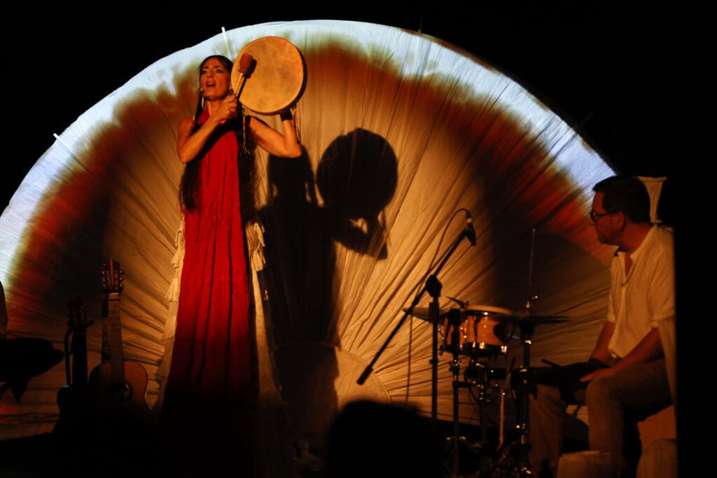 Christina Rosmini en robe rouge, tambourin à la main, sous les lumières de la scène